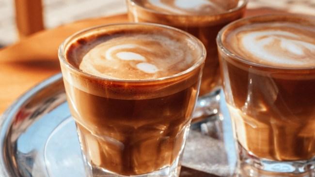 Selective focus three glasses with coffee with milk foam on a metal tray in coffee shop in sunny day.